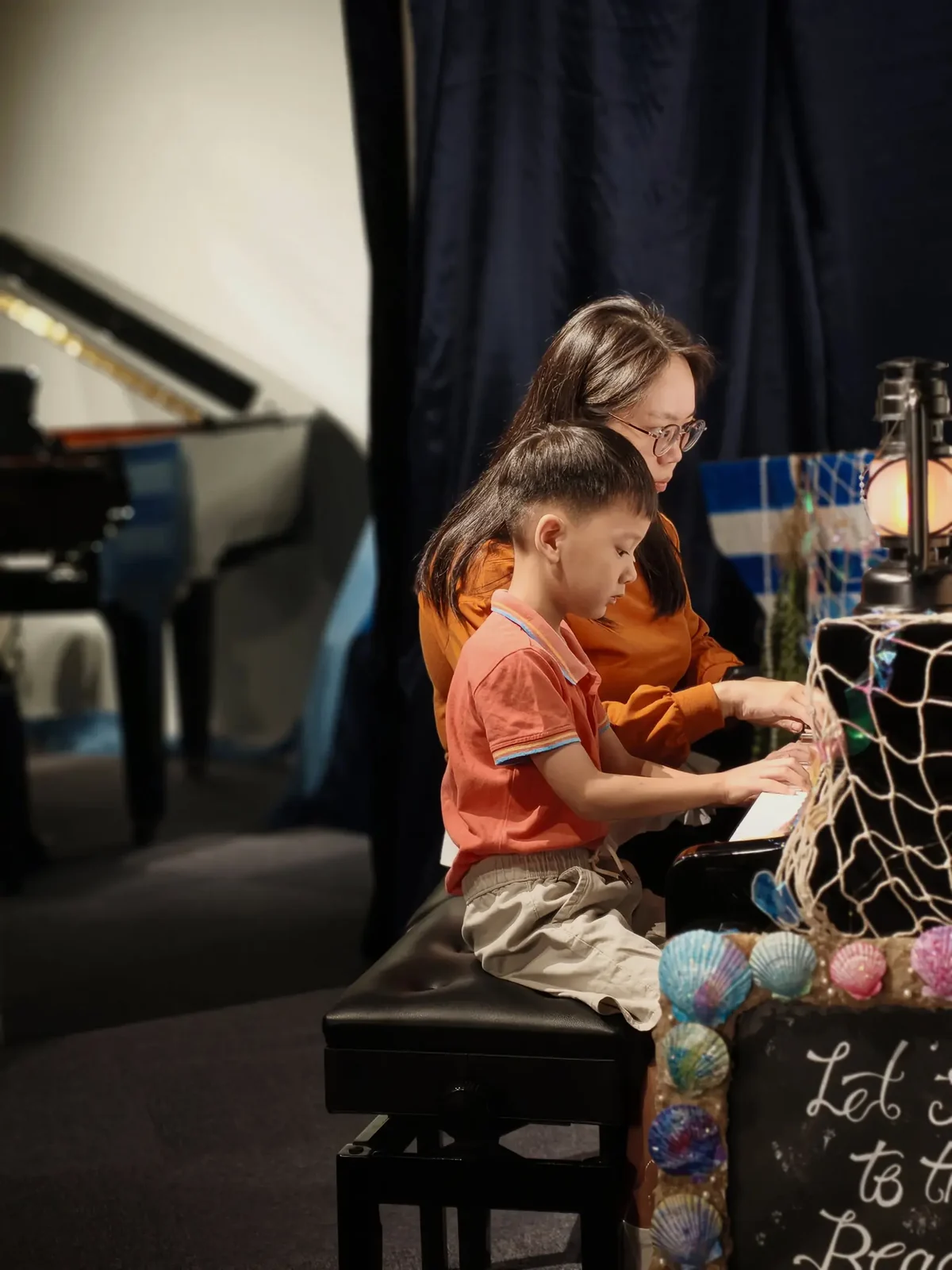 Young FingerGYM graduate performing at the piano with her teacher during the graduation performance