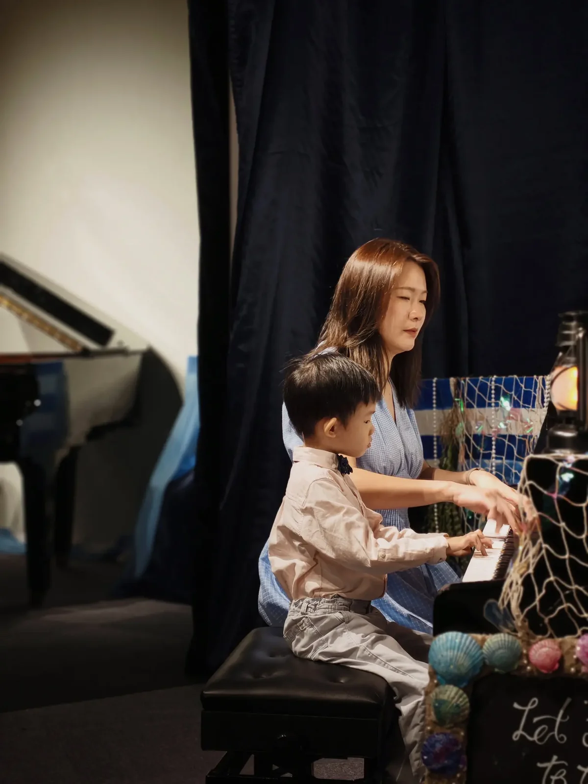 Young FingerGYM graduate performing at the piano beside her teacher