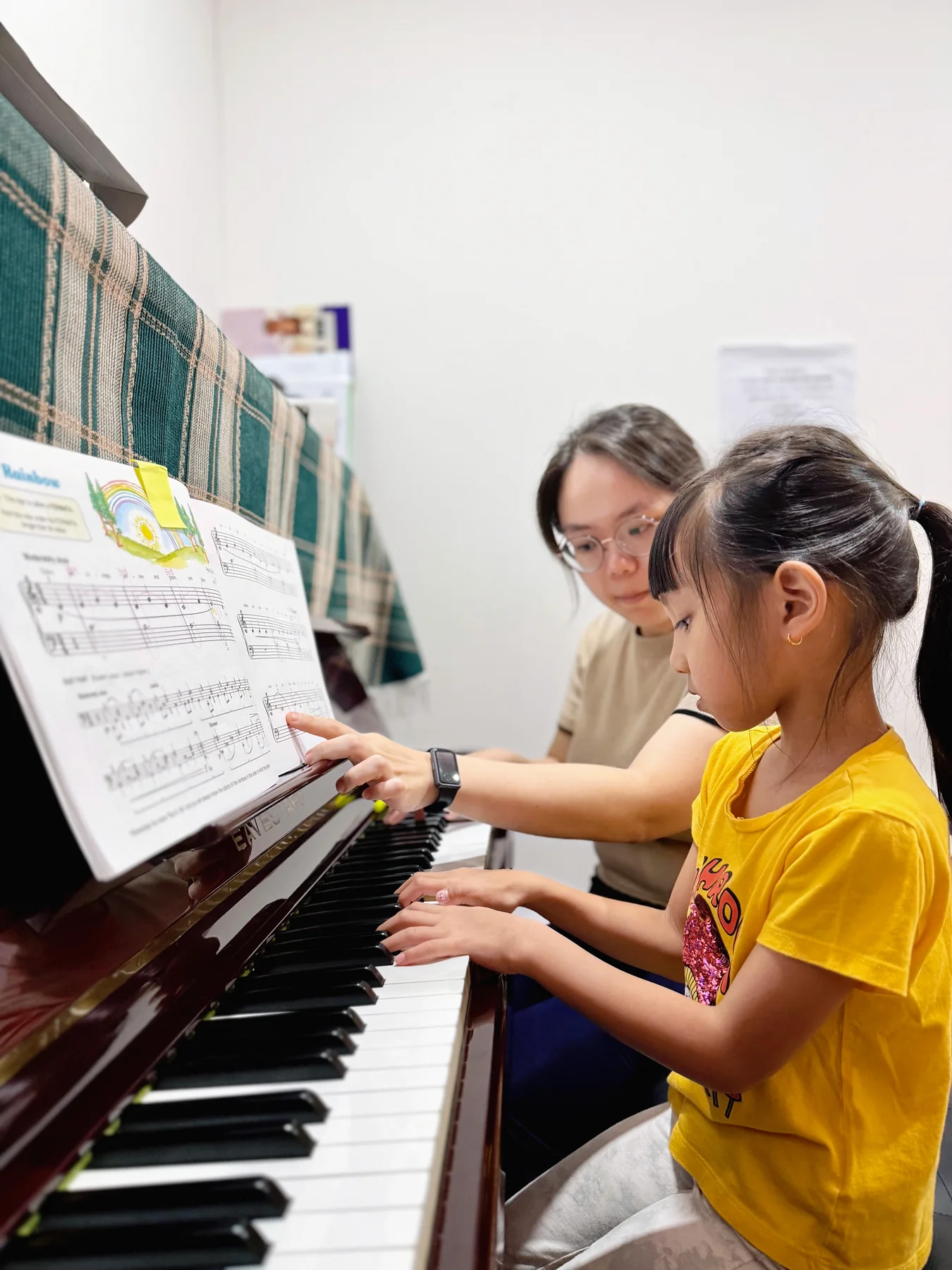 Piano teacher pointing to sheet music while a student plays at the piano